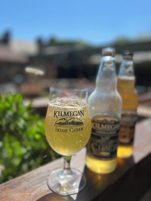 A glass of Kilmegan Irish Cider on a wooden surface with two bottles of the same brand in the background.