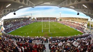 A stadium with a large crowd, a football pitch, and a clear sky.
