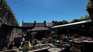 An outdoor seating area with tables and chairs, a brick wall, and a clear blue sky with the sun shining. - Dundrum Inn (Newcastle)