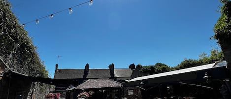 An outdoor seating area with tables and chairs, a brick wall, and a clear blue sky with the sun shining.