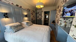 A bedroom with a large bed, two bedside lamps, a television on the wall, and floral wallpaper. - Dundrum Inn (Newcastle)