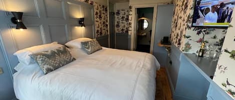 Un dormitorio con una cama grande, dos lámparas de noche, un televisor en la pared y papel tapiz con motivos florales.