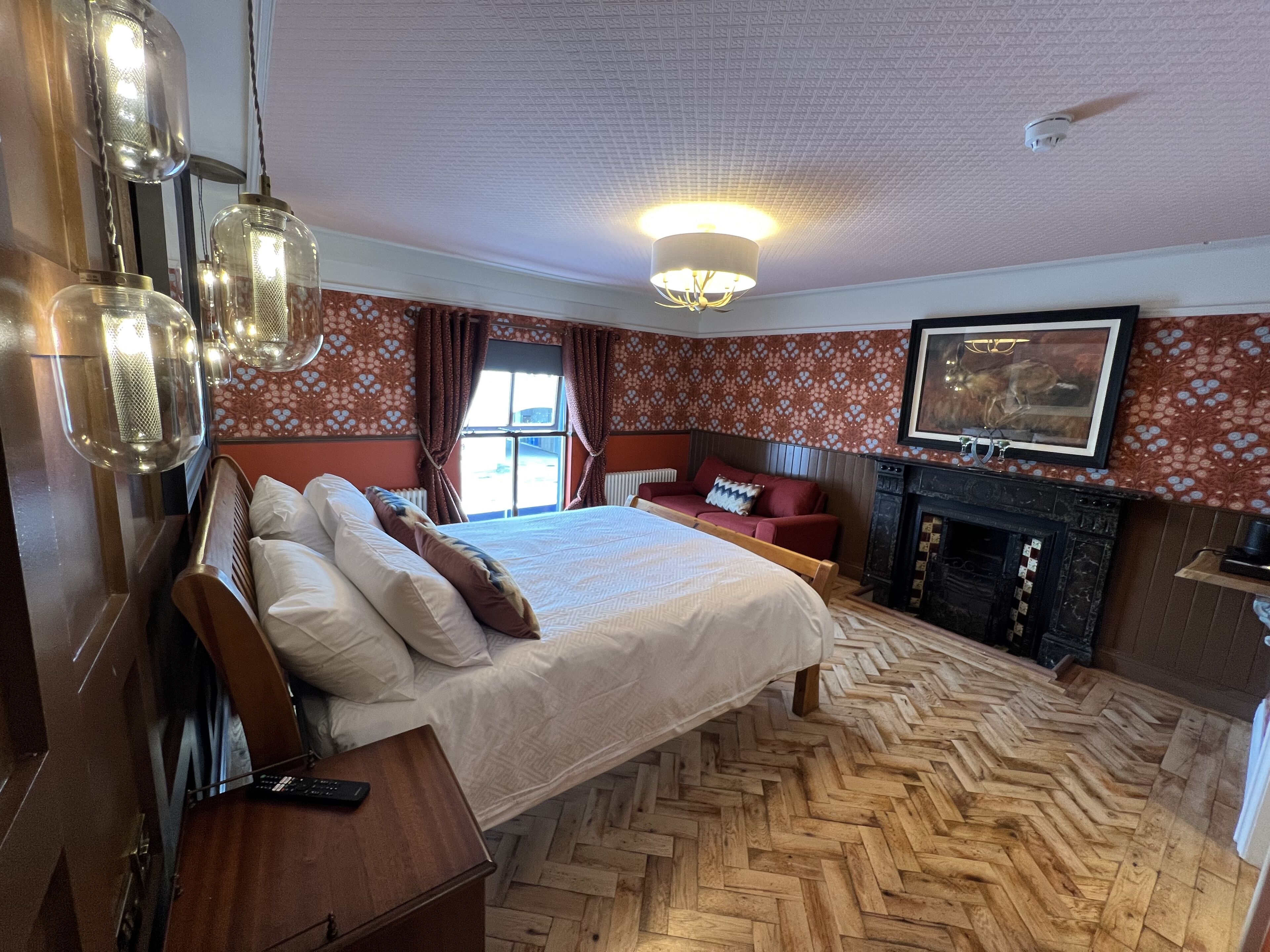 Spaziosa camera da letto con un ampio letto, un camino e un pavimento in legno a motivi a spina di pesce.