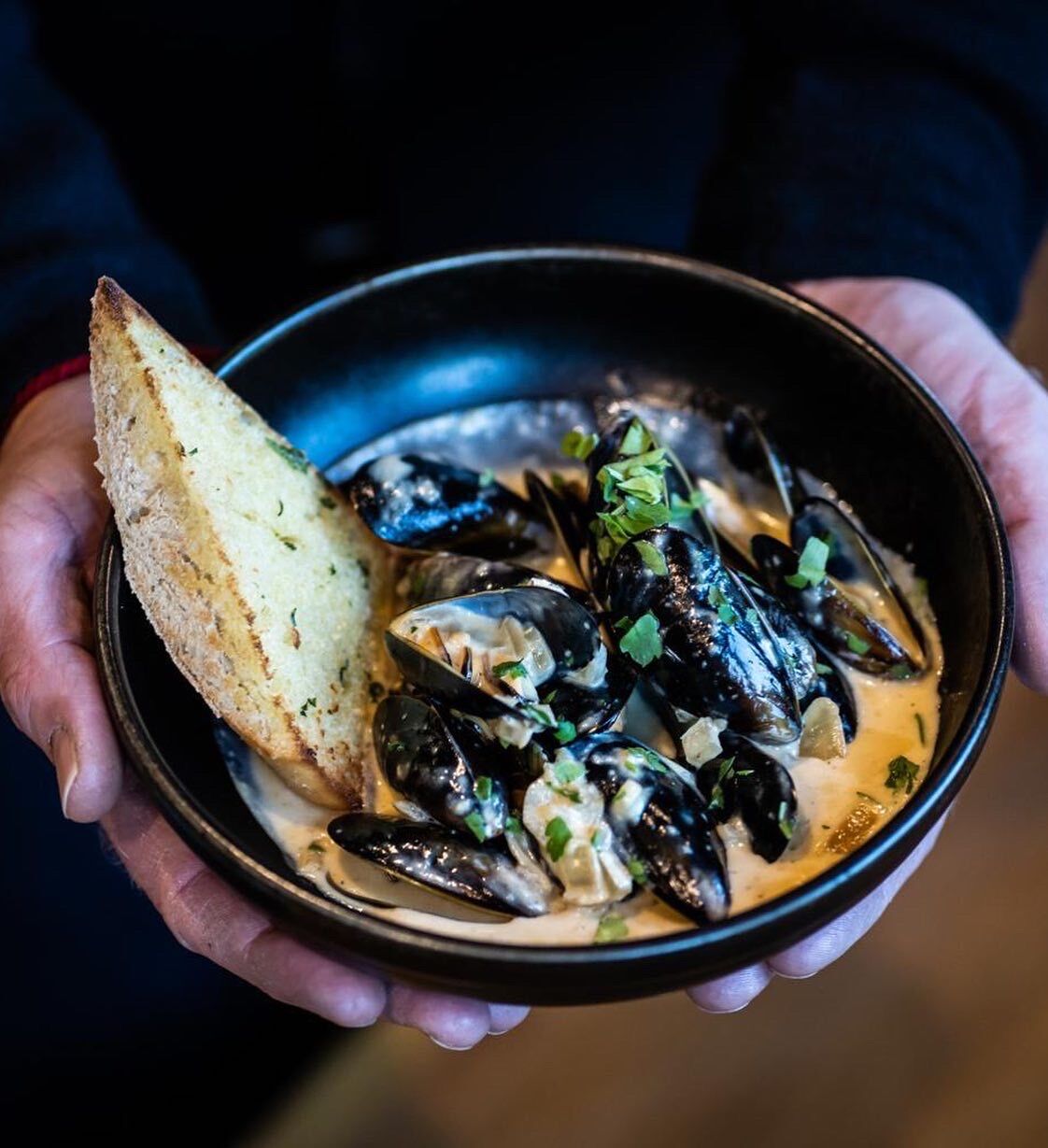 A bowl of mussels with a slice of bread.