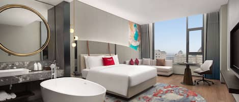 A modern hotel room with a large bed, a round bathtub, a sitting area, and a large window offering a city view.
