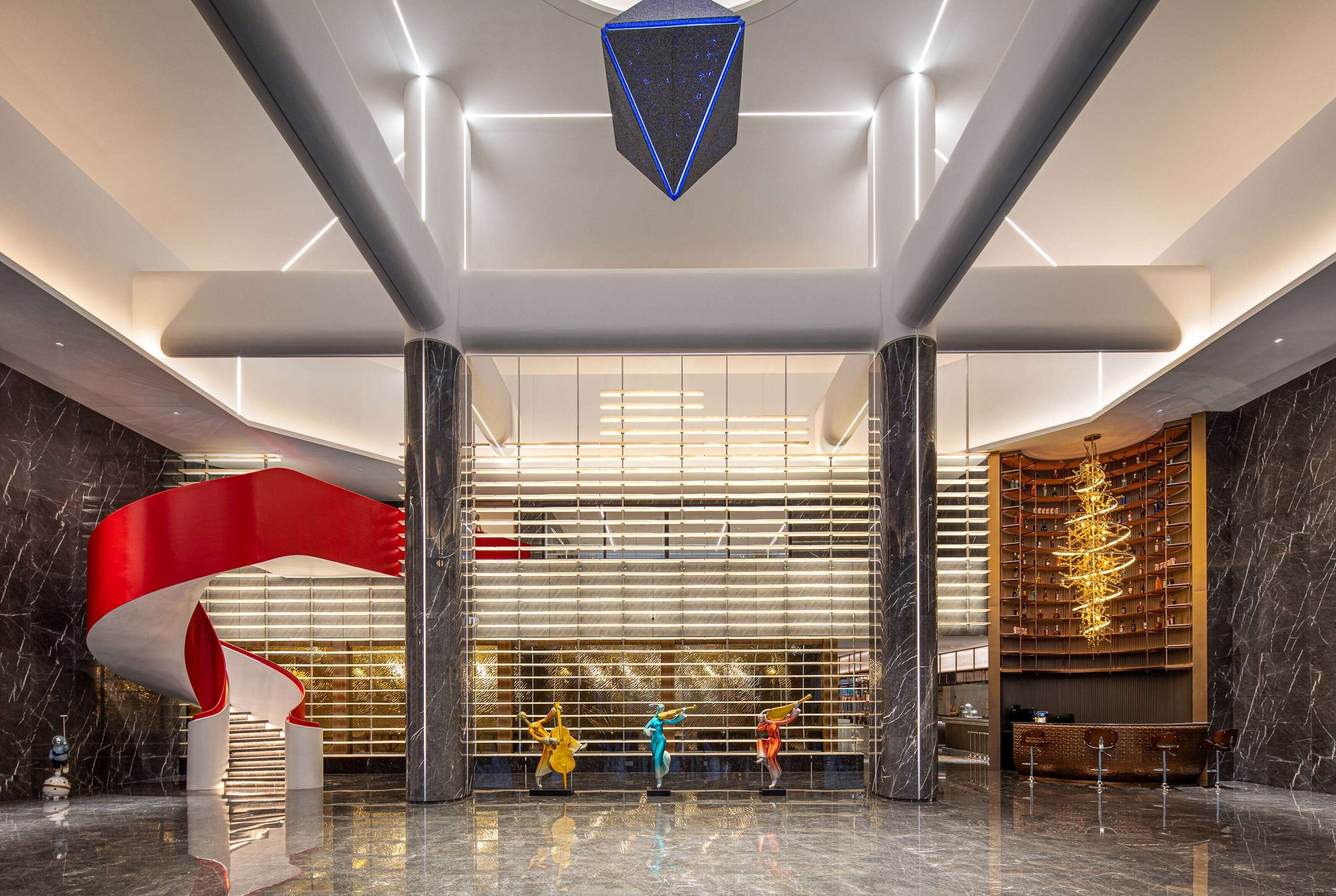 A modern lobby with a central staircase, a large red sculpture, and a library with bookshelves.