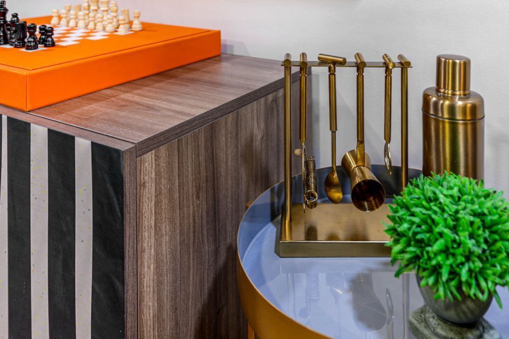 Un meuble en bois surmonté d’un échiquier, une lampe en laiton et une bouteille de couleur dorée, le tout posé sur une table bleue.