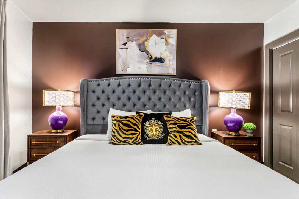 A bedroom with a tufted headboard, a large bed, two nightstands with lamps, and a wall-mounted artwork.