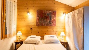 A double bed with white linens, two bedside lamps, and a painting on the wooden ceiling. - 10th floor, view valley, ski locker, 36m², Valmorel (Valmorel)