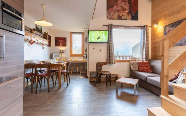 Una sala de estar acogedora con un sofá, una zona de comedor con muebles de madera, un televisor y una escalera.