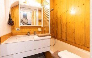 Un baño con pared de madera, un lavamanos blanco, un espejo y una toalla.