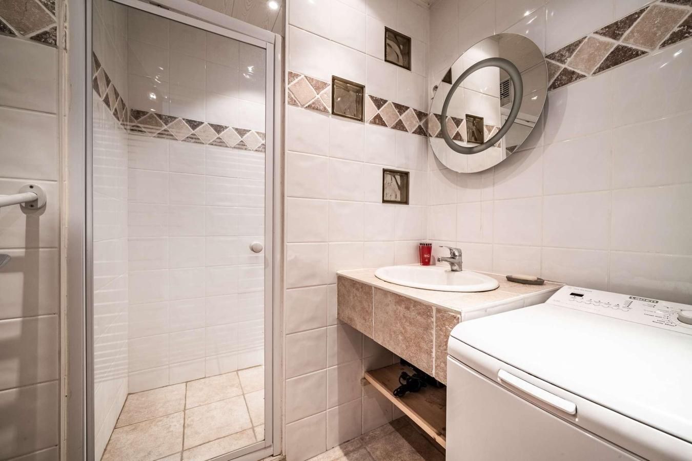 Un bagno con box doccia in vetro, lavabo con specchio e lavatrice bianca.