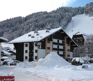 A ski resort building with multiple floors, a sloped roof, and a snow-covered mountain in the background.