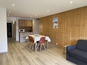 A modern kitchen with wooden cabinets, a dining table with chairs, and a blue sofa in a room with wooden paneling and a tiled floor. - 200m from ski lifts, 2nd floor, view ski slopes, balcony, parking, tv, ski locker, 57m², Morzine (Morzine)