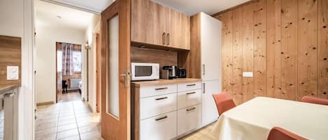 A modern kitchen with wooden cabinets, a microwave, and a coffee maker. There is a dining area with a table and chairs.