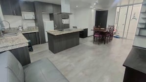 Une cuisine moderne avec des meubles de rangement aux couleurs foncées, un îlot central et un coin repas avec des chaises.