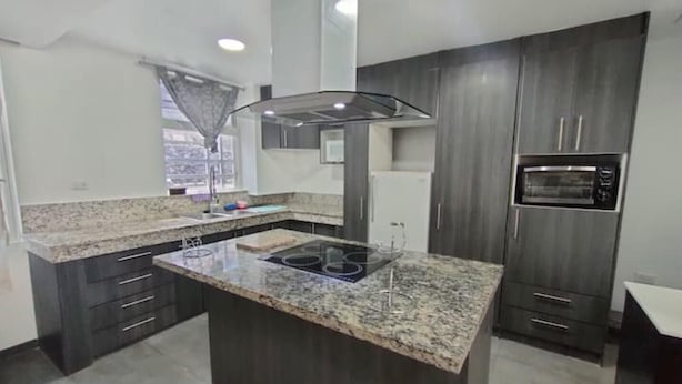 Une cuisine moderne avec des meubles de couleur bois foncé, des plans de travail en granit, une cuisinière encastrée et un four à micro-ondes.