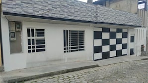 Un bâtiment avec un toit recouvert de tuiles, un garage dont le sol est carrelé avec un motif à carreaux et une rue pavée.