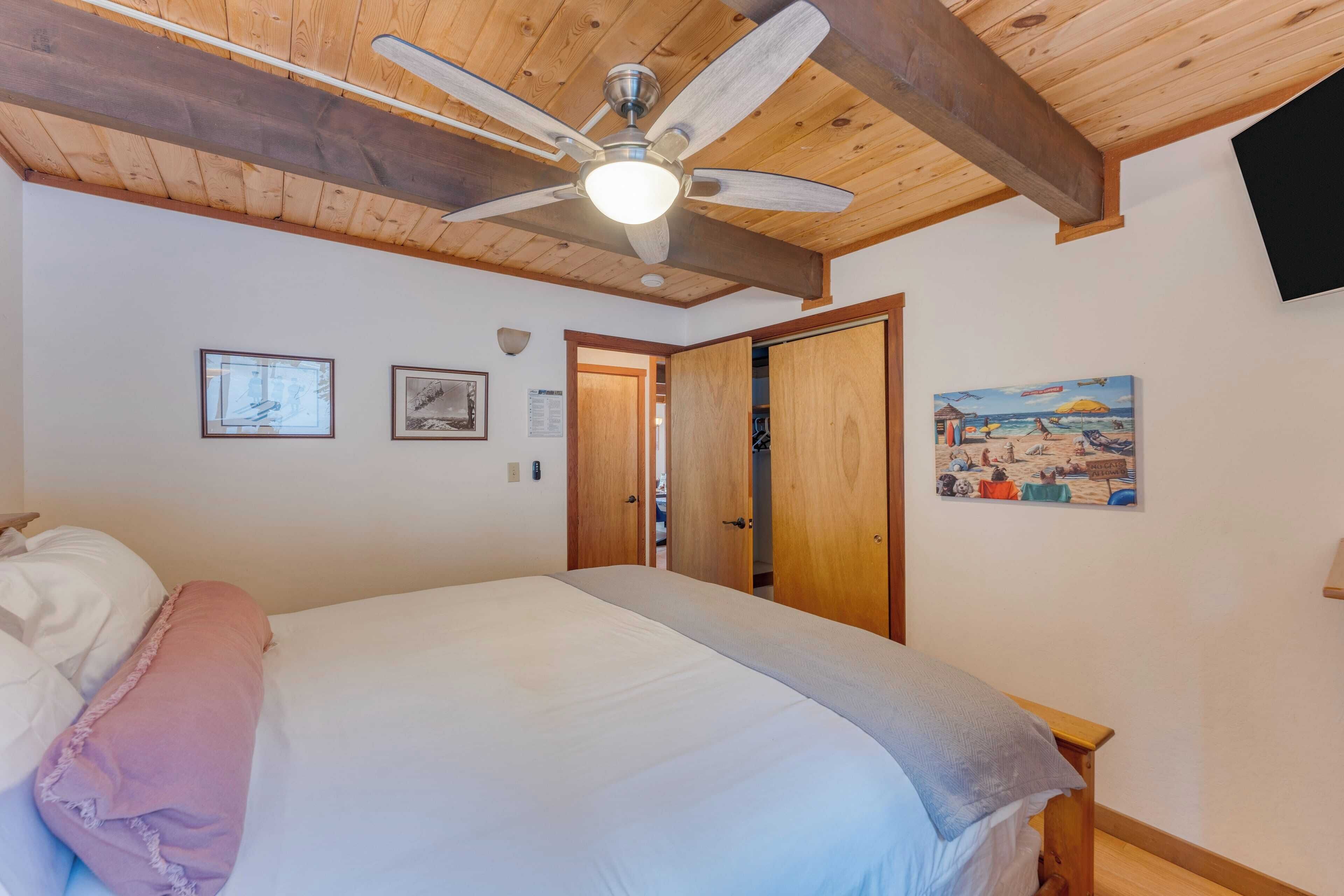 Ein Schlafzimmer mit einem Bett, einem Deckenventilator, Holzbalken und einem Bild an der Wand.