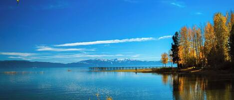 A calm lake with a pier extending into the water, surrounded by trees and mountains in the distance.