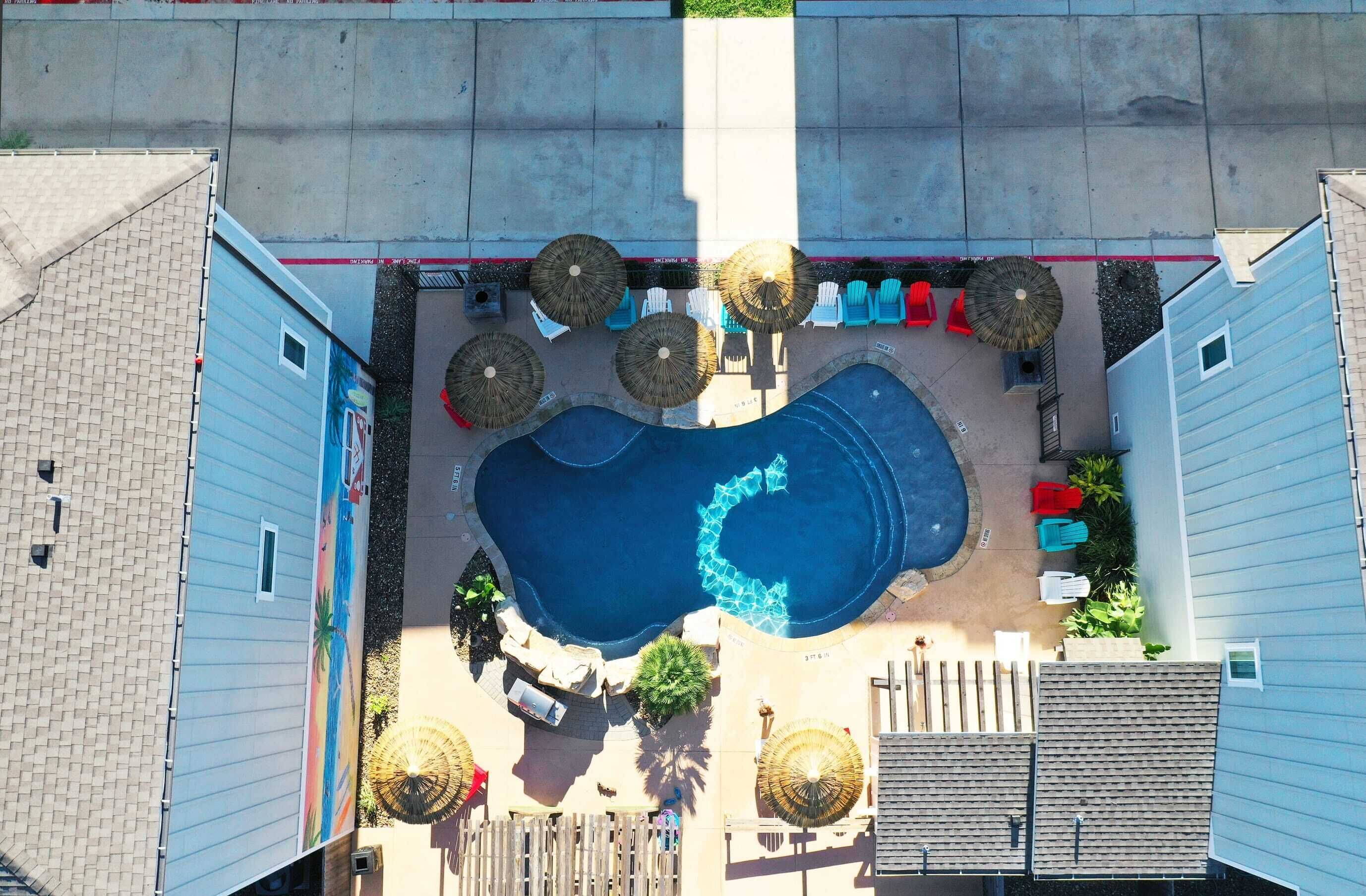 Vue aérienne d’un quartier résidentiel avec une piscine, un espace de détente extérieur et un jardin clos.