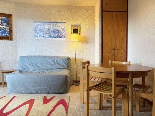 A room with a blue sofa, a wooden dining table with chairs, a lamp, and a door.