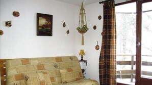 Un salon chaleureux avec un canapé à motifs, une plante suspendue et une fenêtre avec des rideaux.