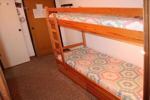 A bunk bed with a ladder, a patterned mattress, and a door with a bulletin board.