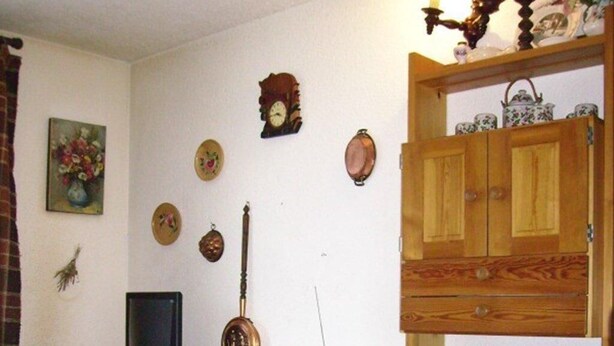 Un coin repas avec une table et des chaises en bois, un téléviseur posé sur un meuble, et divers éléments de décoration murale, notamment des horloges et des assiettes.