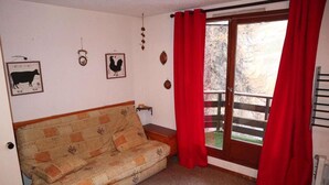 Une pièce chaleureuse avec un canapé, une porte en bois et une fenêtre ornée de rideaux rouges.