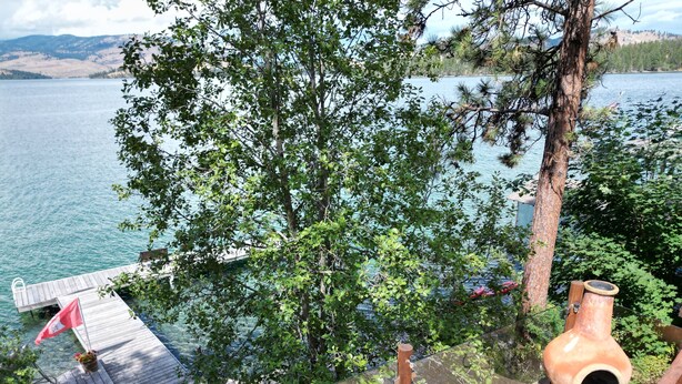 A wooden deck overlooking a lake with a glass balustrade, a rustic clay pot, and a flag. - Ultimate Lakeside Retreat on Flathead Lake near Glacier National Park (Big Arm)