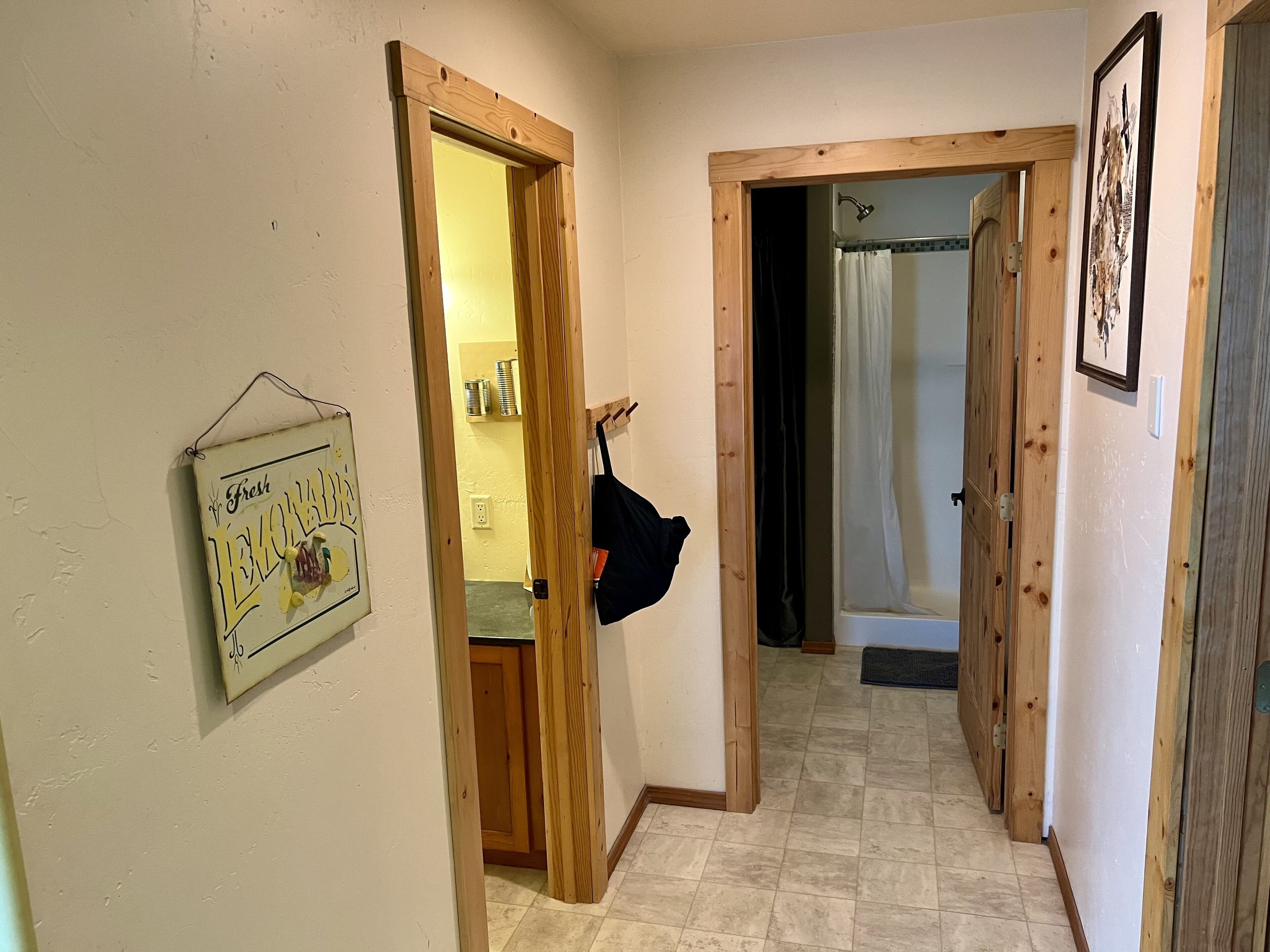 A narrow hallway with wooden doors leading to a bathroom. A black bag hangs on one door, and a framed picture is on the wall.