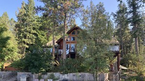 A cabin with a deck, surrounded by trees, and a wooden fence. - Ultimate Lakeside Retreat on Flathead Lake near Glacier National Park (Big Arm)