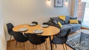 A dining area with a round wooden table, black chairs, and a grey sofa with yellow cushions.