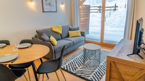 A cozy living room with a grey sofa, a round wooden table, and a TV stand.