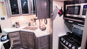 Une cuisine avec des meubles de couleur bois foncé, un four à micro-ondes en acier inoxydable, une cuisinière et un évier.