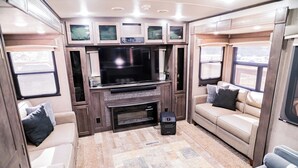 Un intérieur de camping-car confortable, doté d’un grand téléviseur, d’un coin salon et d’une cheminée.