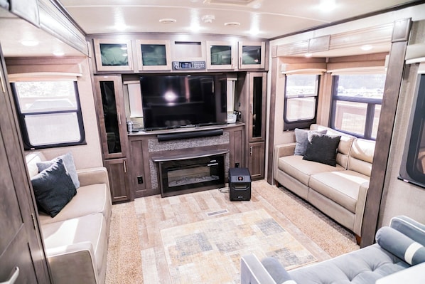 Un interior de autocaravana acogedor con un televisor grande, zona de estar y una chimenea.