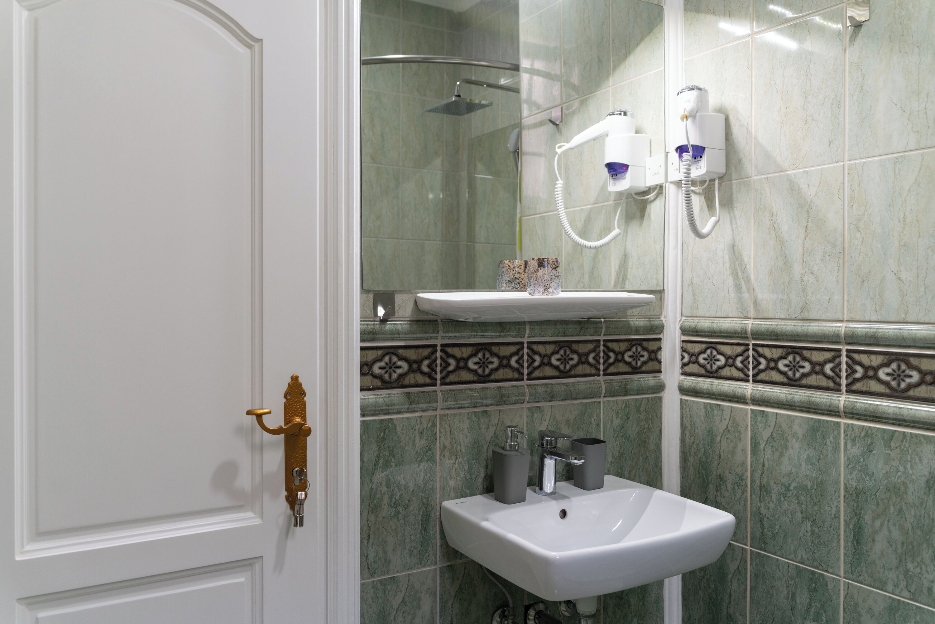 Un baño con lavamanos blanco, cabina de ducha de vidrio y un salpicadero decorado con azulejos.