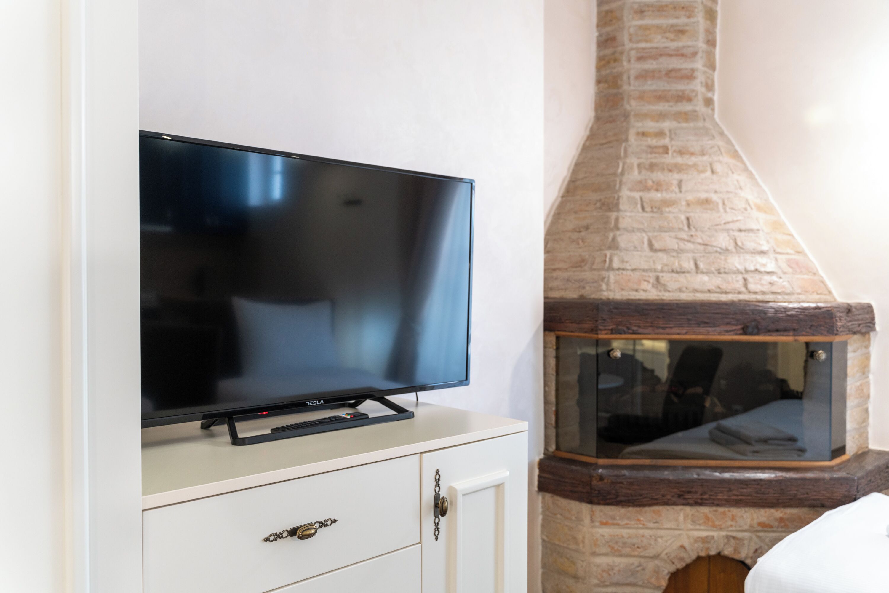 A flat-screen TV on a white cabinet, a stone fireplace with a glass viewing window, and a wooden door.