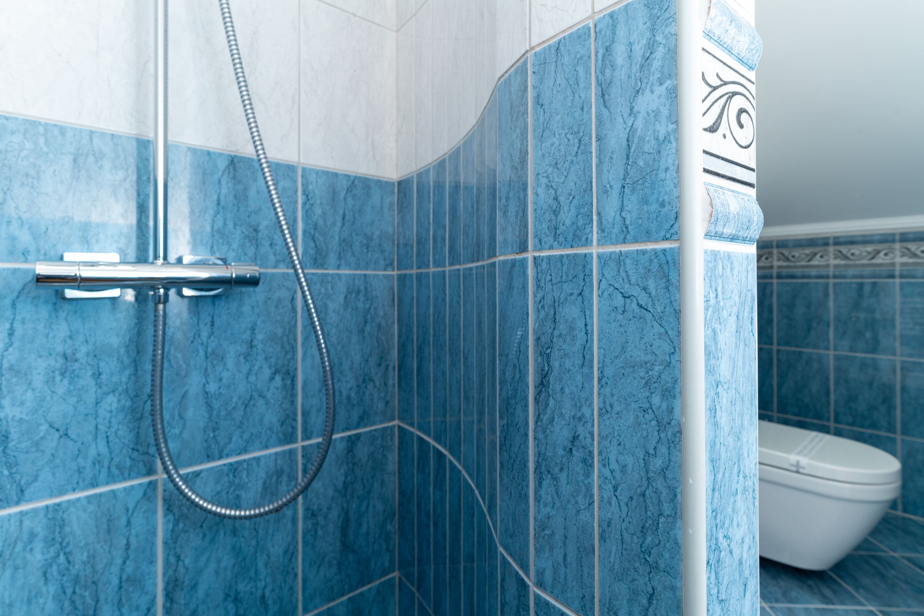 A bathroom with blue marble tiles, a shower with a handheld hose, and a toilet.