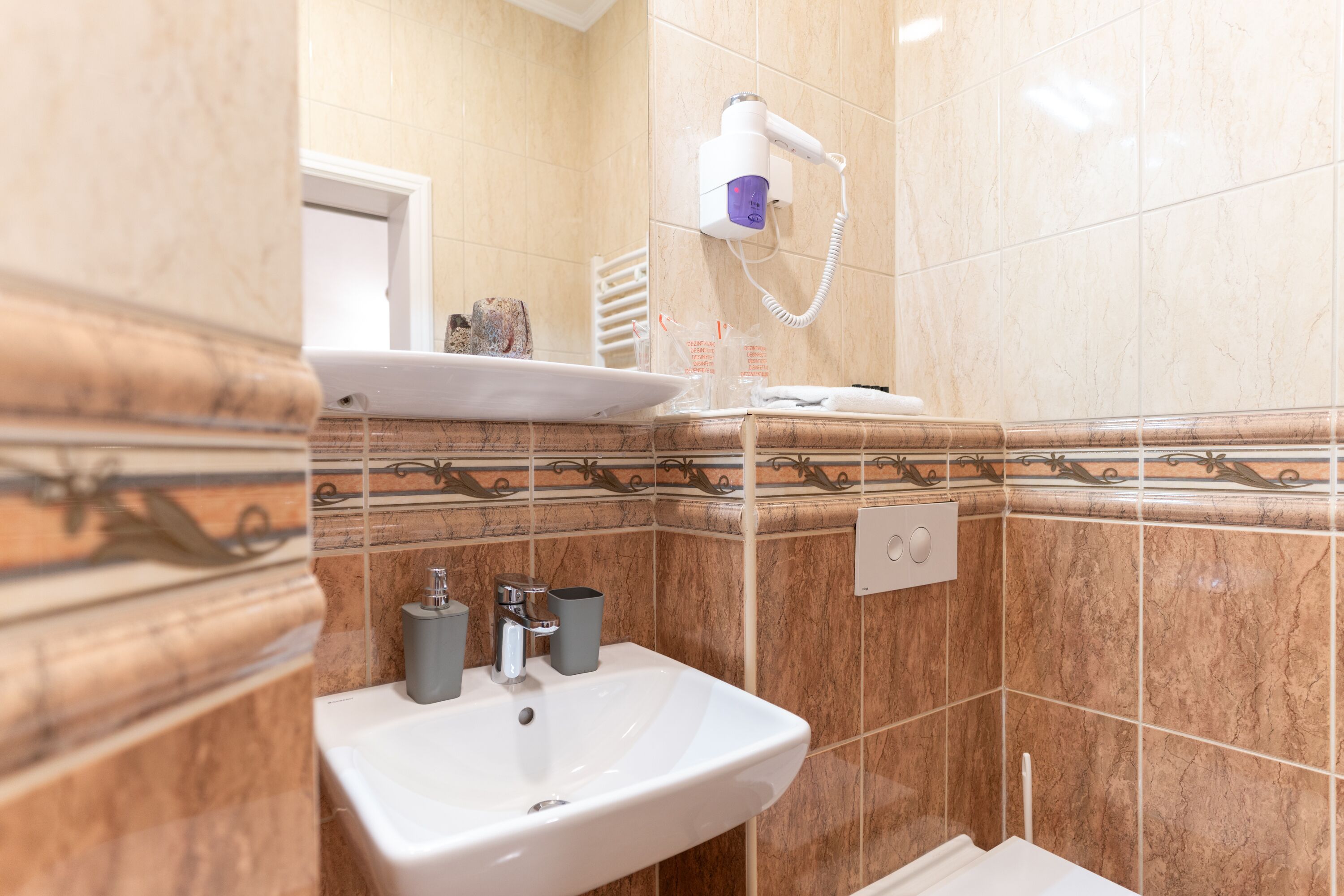 Ein Badezimmer mit Waschbecken, Spiegel, Handtuchhalter und einem an der Wand montierten Föhn.