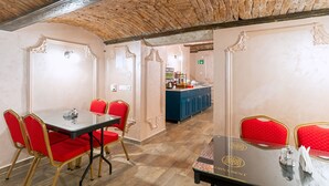 A dining area with a brick ceiling, red upholstered chairs, a glass table, and a blue counter in the background. - Ornament Hotel (Sarajevo)