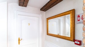 A white door with a golden handle and the number 9 on it, a gold-framed mirror on the wall, and a red emergency exit sign. - Ornament Hotel (Sarajevo)