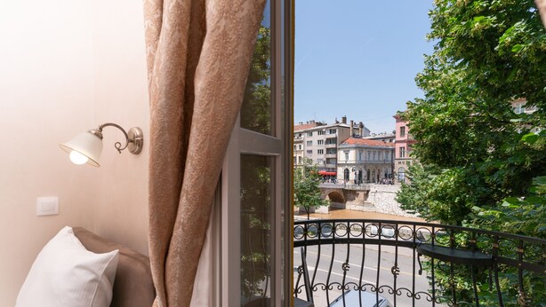 A balcony with a wrought iron railing, a view of a city street, and a building with a sign that reads "MU". - Ornament Hotel (Sarajevo)