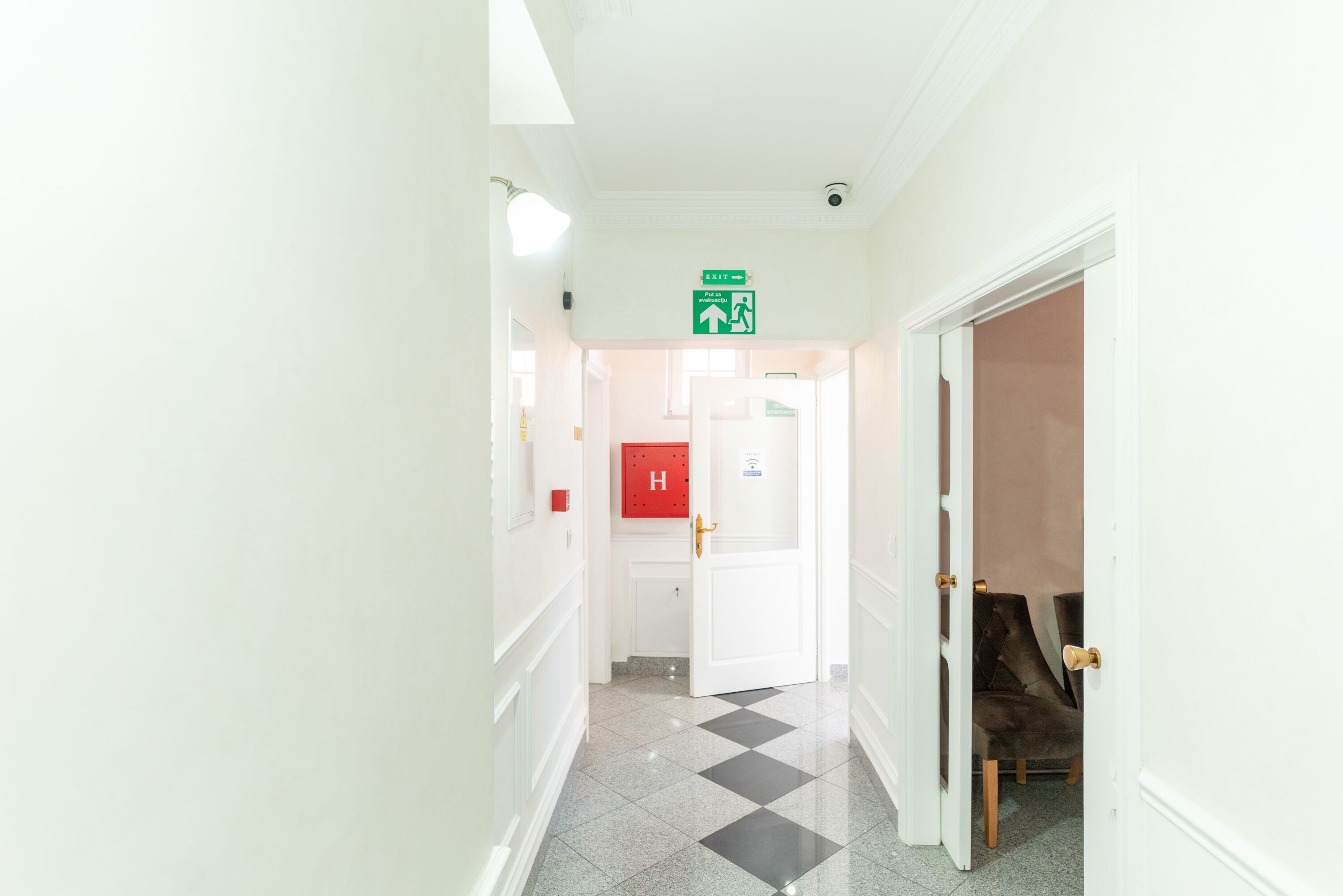 A hotel hallway with a check-in desk, a fire alarm, and a door leading to a room.