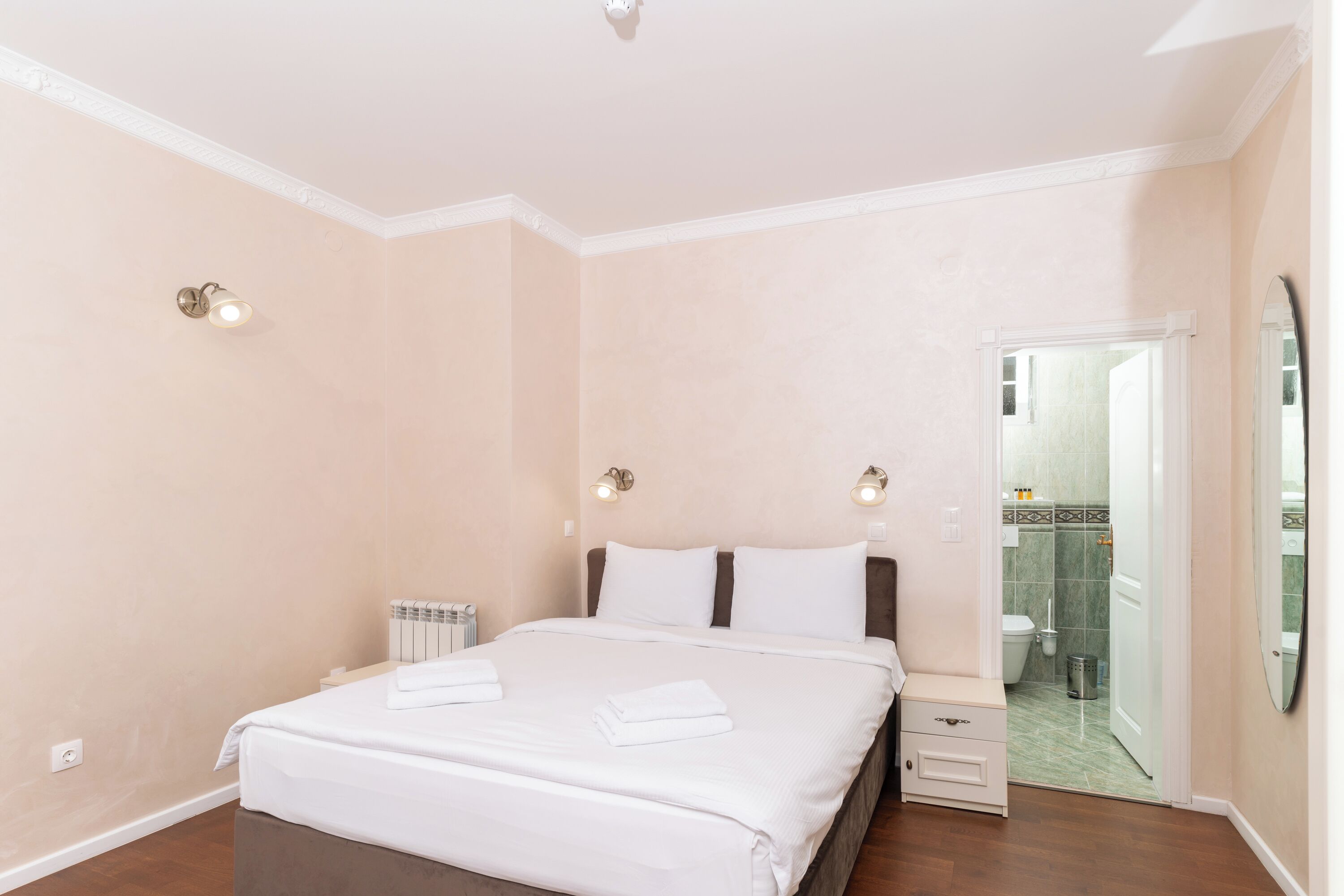 A bedroom with a bed, bedside tables, a radiator, and a bathroom visible through an open door.