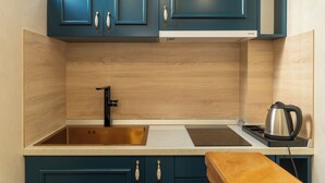 A kitchen with blue cabinets, a stainless steel sink, a black kettle, and a wooden countertop. - Ornament Hotel (Sarajevo)