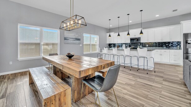 A modern kitchen with white cabinets, a wooden dining table, and pendant lights. - The Blue Escape- 5BR/2.5BA, Huge Private Pool and Hot Tub. Steps to the Beach (Panama City)
