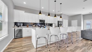 A modern kitchen with white cabinets, a central island, and bar stools. - The Blue Escape- 5BR/2.5BA, Huge Private Pool and Hot Tub. Steps to the Beach (Panama City)